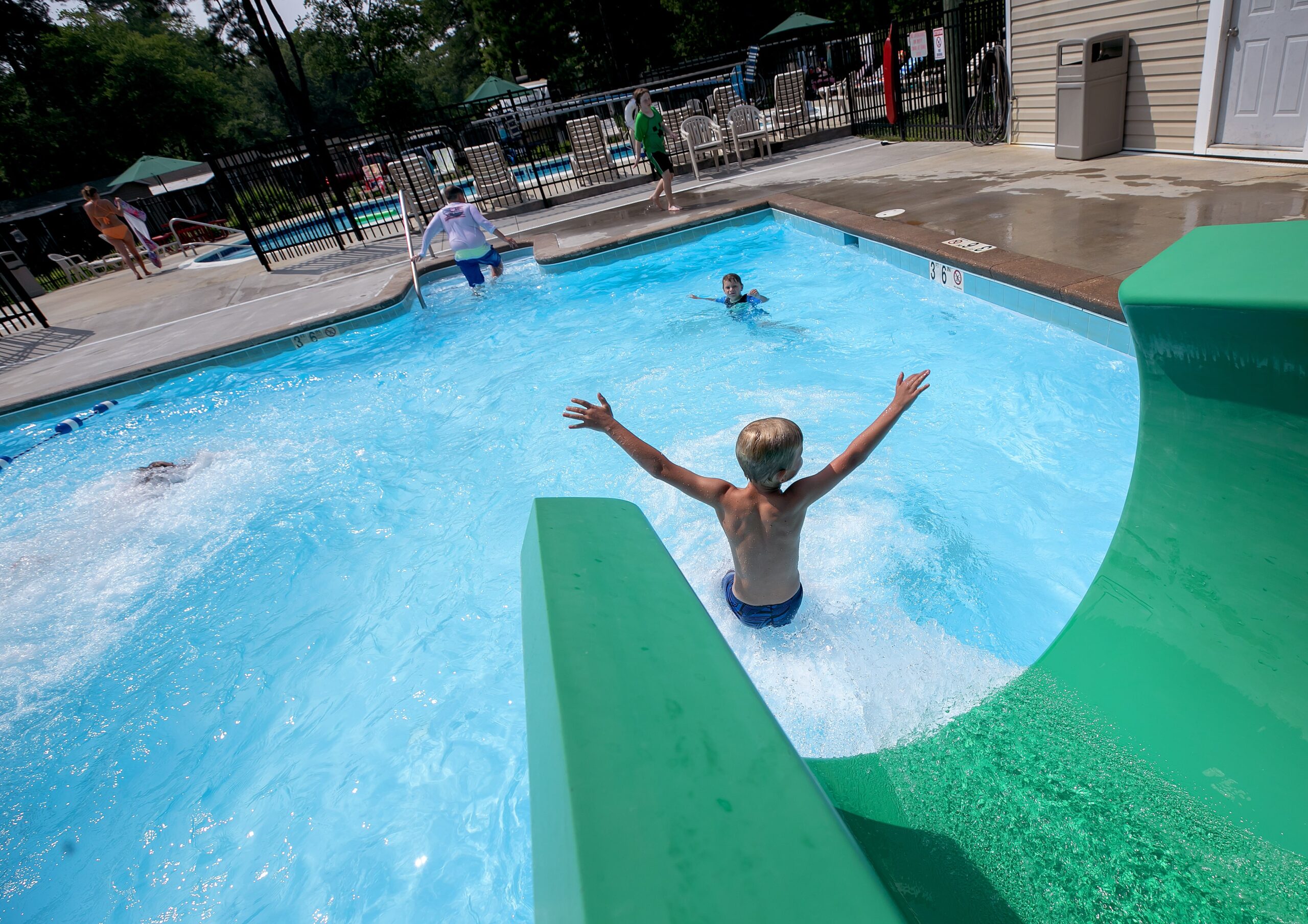 A child joyfully splashes into the pool from a green water slide at Camp Cardinal, enjoying summer fun at the campground.