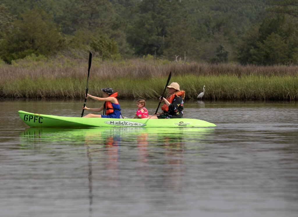 Family in a green kayak paddling near grassy shoreline