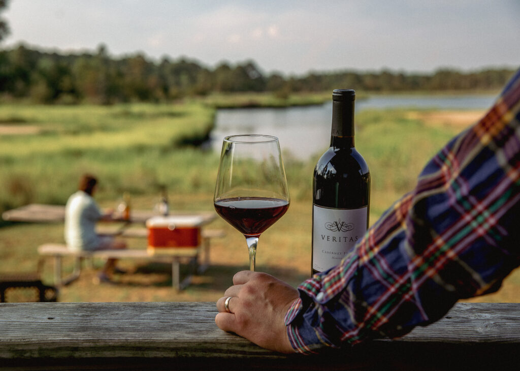 A glass and bottle of wine on a railing with a blurred picnic scene in the background