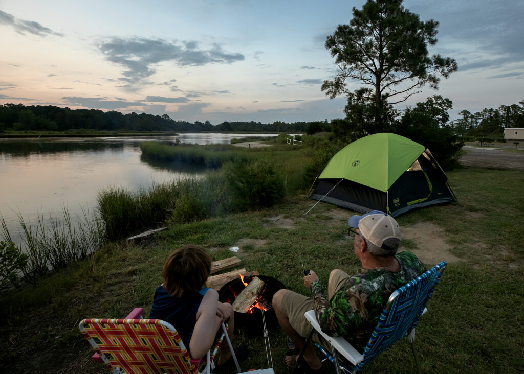 Family sitting by fire with tent near riverbank