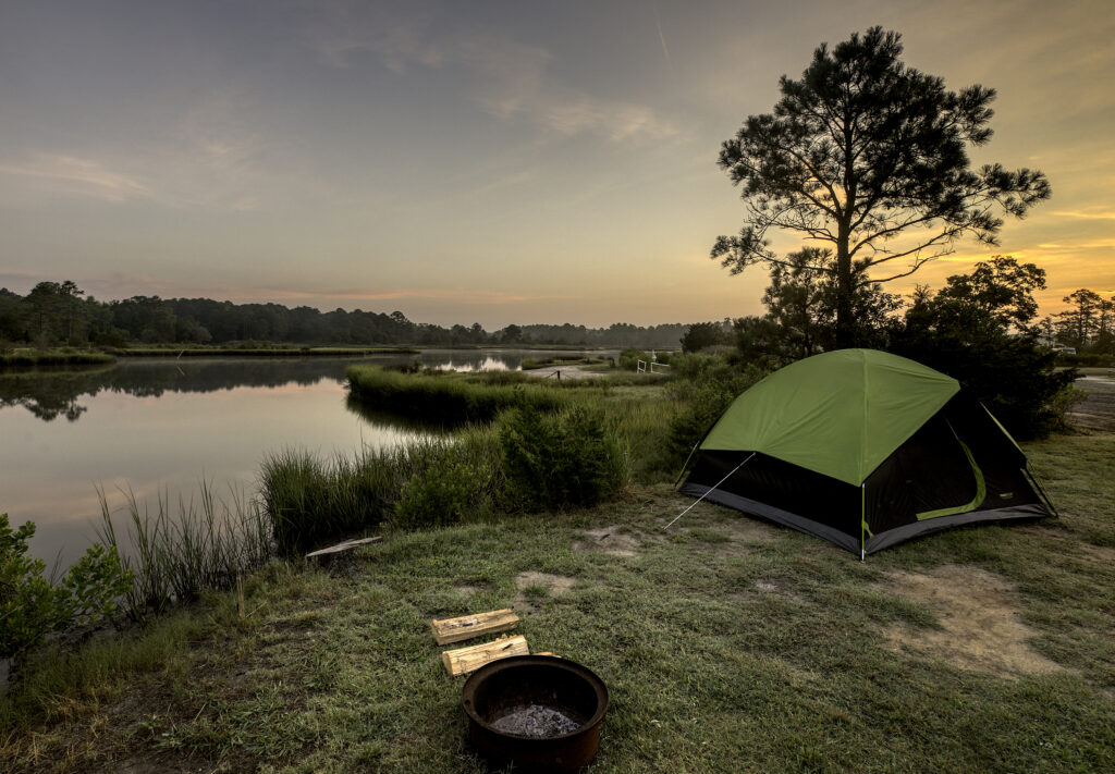 Tent and firepit near shoreline under a vibrant sky.