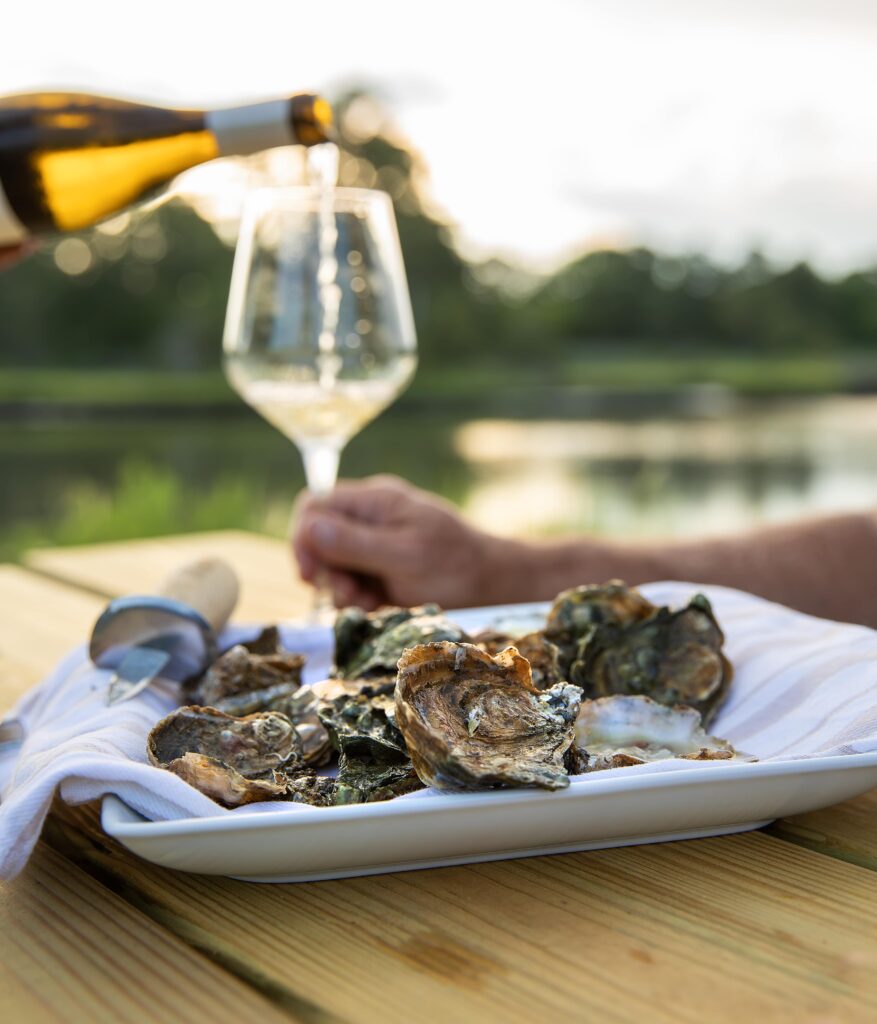 White wine being poured beside a plate of fresh oysters on a dockside table at sunset in Virginia