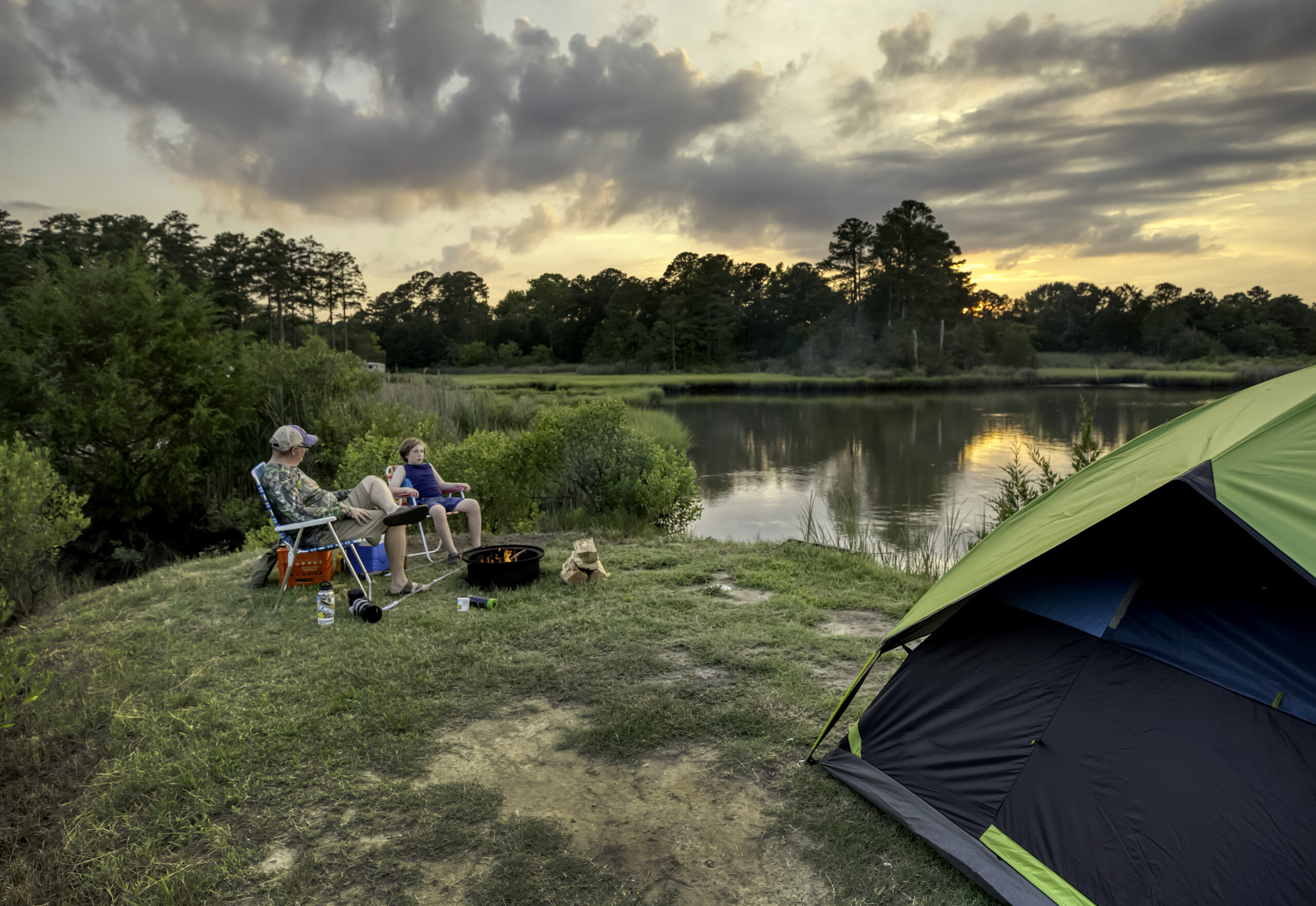 A green tent beside a campfire near the water during sunset at Camp Cardinal.